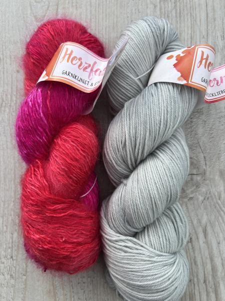 Zwei Stränge handgefärbte Wolle: links Herzfasern No. 50 „Rendezvous in Love“ in leuchtenden Pink- und Rottönen mit Mohairstruktur, rechts Herzfasern No. 11 „Silber White“ in hellem, kühlem Silbergrau auf glatter Merino-Basis. Fotografiert auf hellem Holz